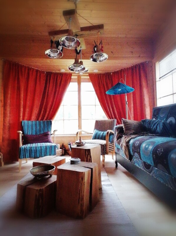 A cozy living room with a wooden ceiling, red curtains, a blue sofa, and a patterned armchair. - Stylish 2 Bdr. cottage, with sauna and all the necessary commodities (Österhankmo)