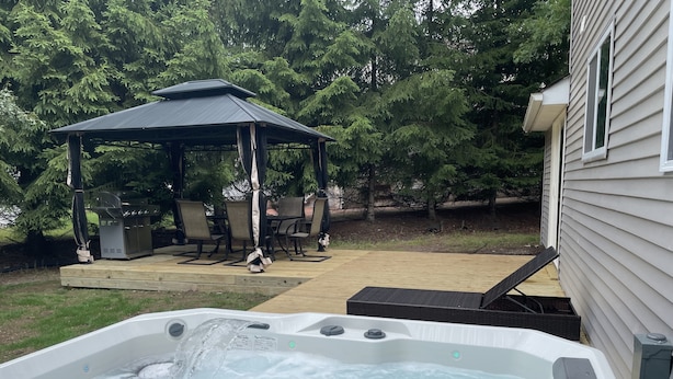 A hot tub with water flowing, a covered patio area with chairs, and a grill. - One of the kind fully loaded house located walking distance from cozy lake (Albrightsville)