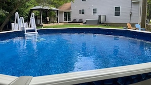 An outdoor swimming pool with a built-in ladder, surrounded by a grassy yard and a house in the background. - One of the kind fully loaded house located walking distance from cozy lake (Albrightsville)
