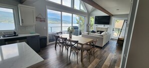A modern kitchen with a dining area, large windows, and a flat-screen TV. - Lakeview Cottage with Pool and Hot Tub (West Kelowna)