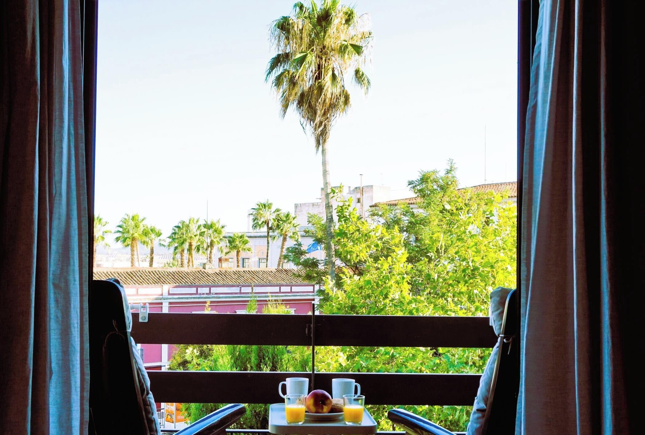 Un balcon avec une table dressée pour le petit-déjeuner, d’où l’on peut admirer un paysage urbain avec des palmiers et des immeubles.