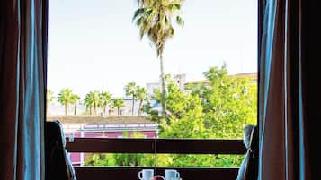 Un balcon avec une table dressée pour le petit-déjeuner, d’où l’on peut admirer un paysage urbain avec des palmiers et des immeubles.
