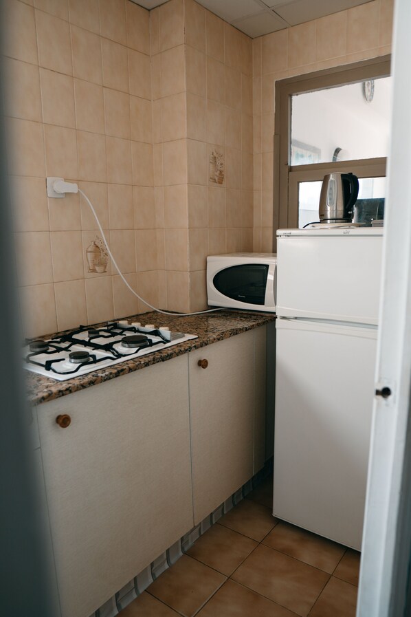 Een kleine keuken met een gasfornuis, magnetron en een witte koelkast.