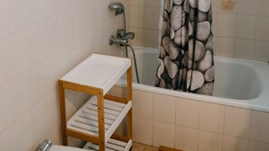 Ein Badezimmer mit einer Badewanne, einer Duschvorhang, einer kleinen Holzablage und einem weißen Waschbecken.
