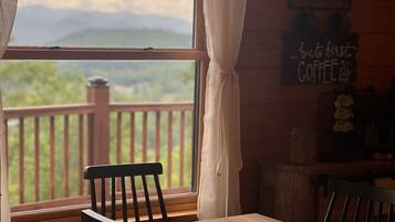 Une table et des chaises en bois près d’une fenêtre donnant sur une terrasse et des montagnes. Une pancarte sur le mur indique : « mais avant tout, du CAFÉ ».