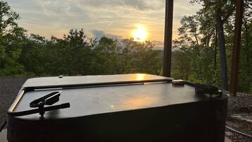 Un espace extérieur abrité, doté d’une table et de chaises, entouré d’arbres et offrant une vue sur le coucher de soleil.