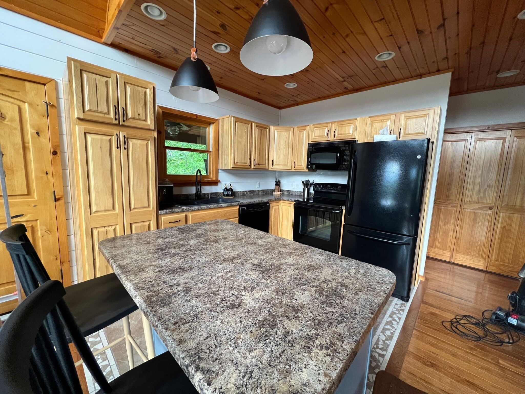 A kitchen with wooden cabinets, granite countertops, a black refrigerator, and a microwave.