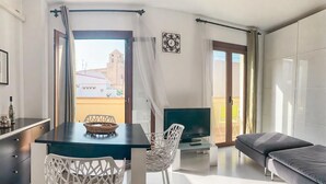 Un salon moderne comprenant un coin repas, un canapé, un téléviseur et un balcon agrémenté de rideaux.