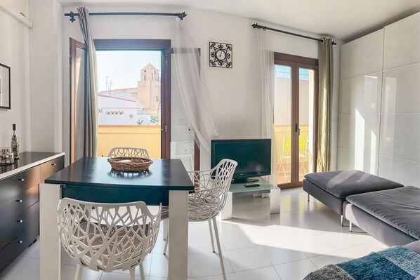 Ein modernes Wohnzimmer mit Essbereich, einer Couch, einem Fernseher und einem Balkon mit Vorhängen.