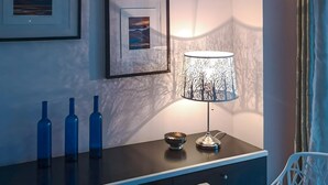 Une pièce moderne avec un bureau en bois foncé, trois bouteilles bleues, une lampe dont l’abat-jour est orné d’un motif d’arbre, et deux tableaux encadrés accrochés au mur.