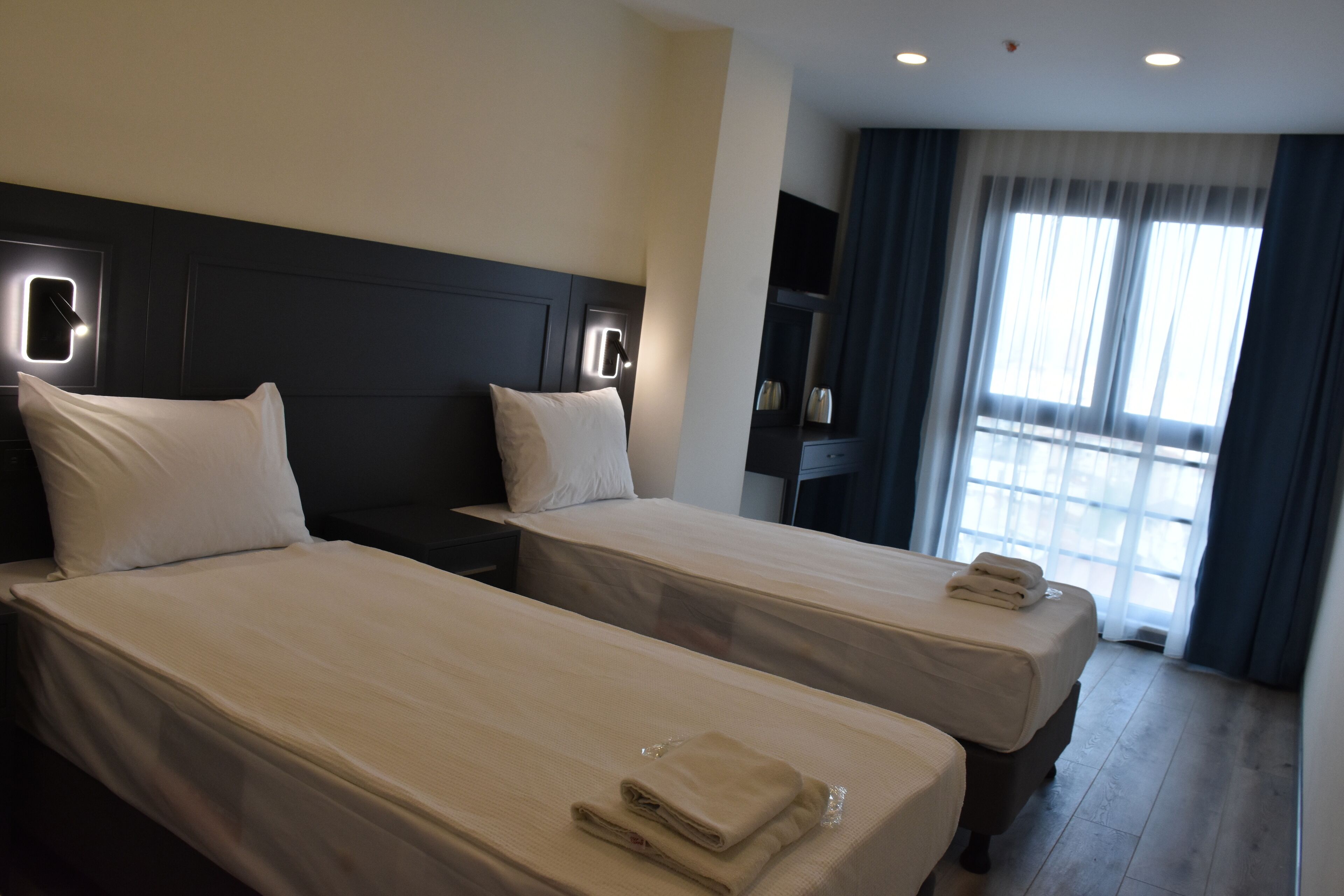 A hotel room with two beds, a TV, a desk, and a window with curtains.