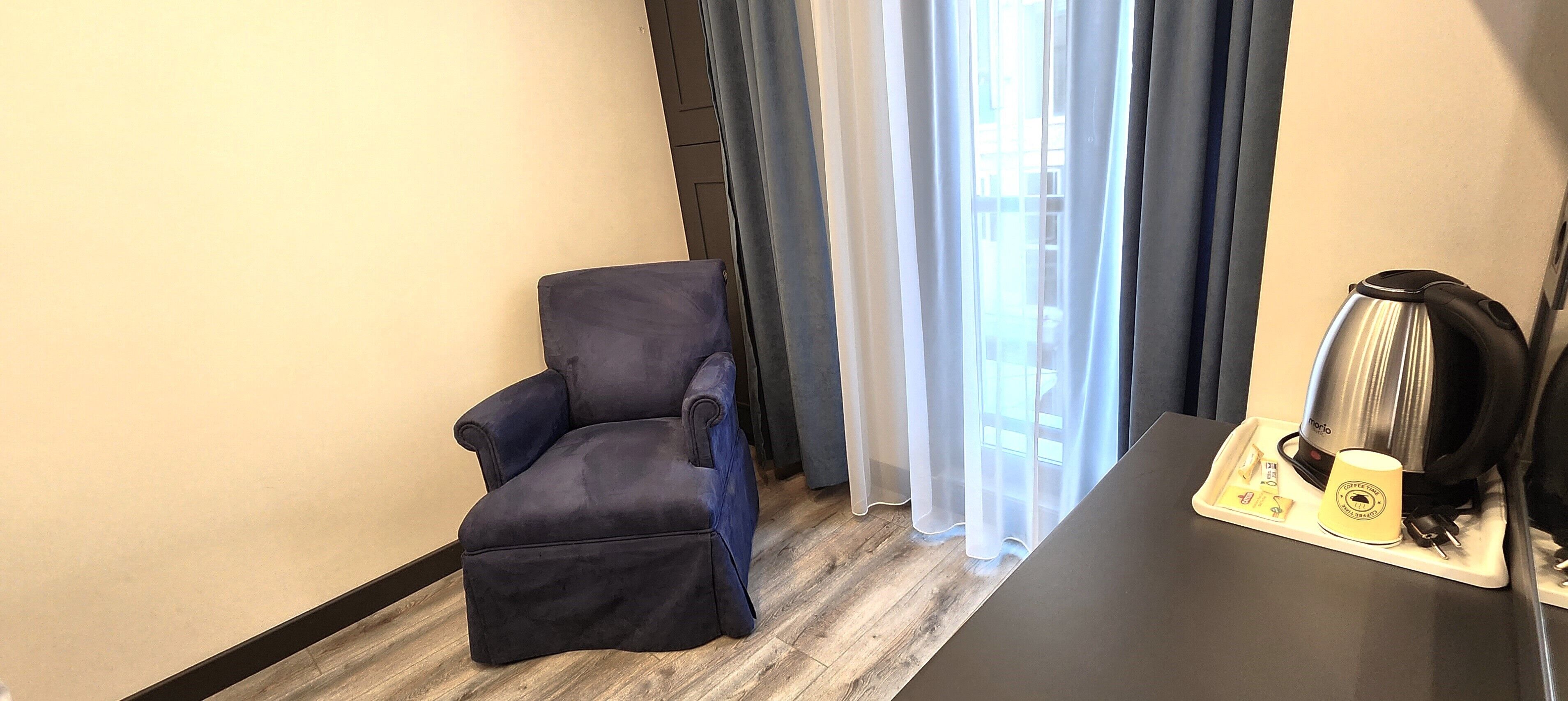 Una habitación con un sillón azul oscuro, una cafetera y una bandeja con una taza de café y sobres de azúcar.