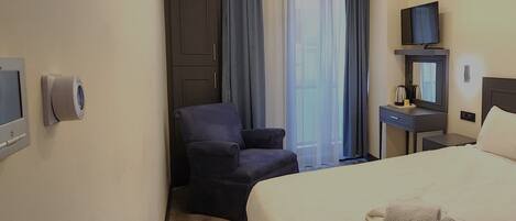 A hotel room with a bed, a chair, a TV, a coffee maker, and a window with curtains.