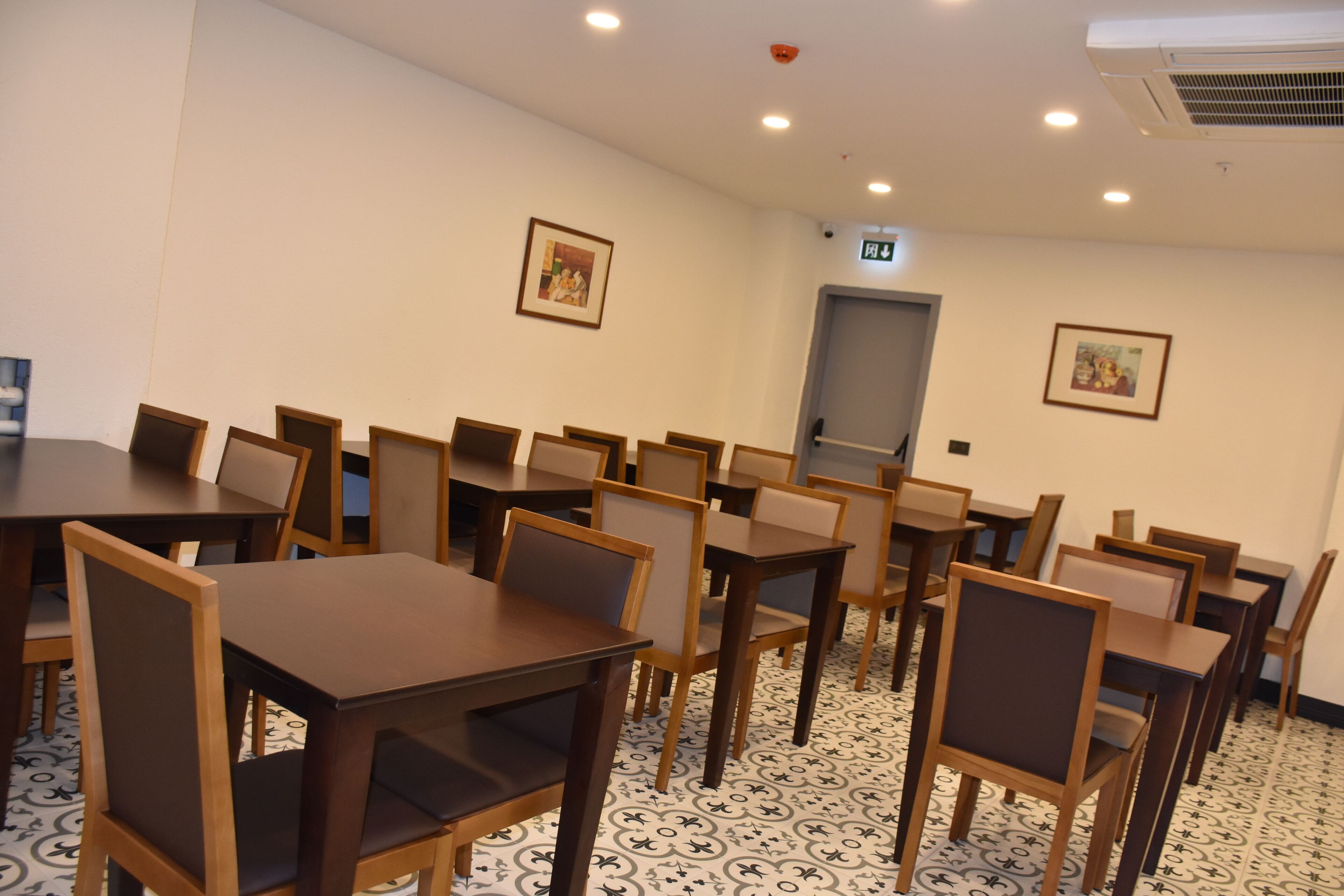A conference room with multiple tables and chairs, a patterned floor, and framed pictures on the walls.
