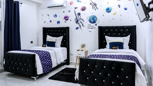 A bedroom with two beds, a ceiling fan, a wall-mounted TV, and a space-themed wall decal.