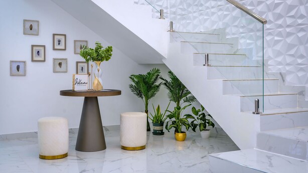 A modern interior with a marble floor, a round table with a welcome sign, and a staircase with a geometric wall design.