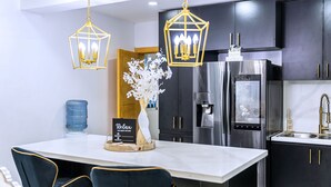 A modern kitchen with dark cabinets, stainless steel appliances, and two hanging pendant lights.