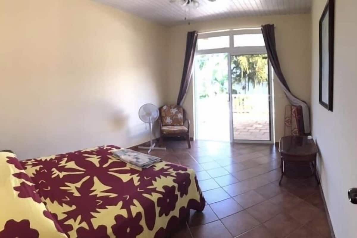 Une pièce comprenant un lit, une chaise, un ventilateur et une porte donnant sur un espace extérieur.