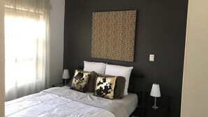 A bedroom with a bed, two bedside tables, a ceiling fan, and a wall-mounted artwork. - Wisteria Place (Plympton)