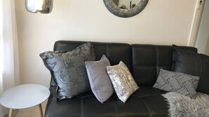 A black leather sofa with patterned cushions, a round mirror, and a pendant light. - Wisteria Place (Plympton)