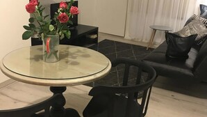 A dining area with a round glass table, two black chairs, a vase with red roses, a small black side table, and a black sofa with a pillow. - Wisteria Place (Plympton)