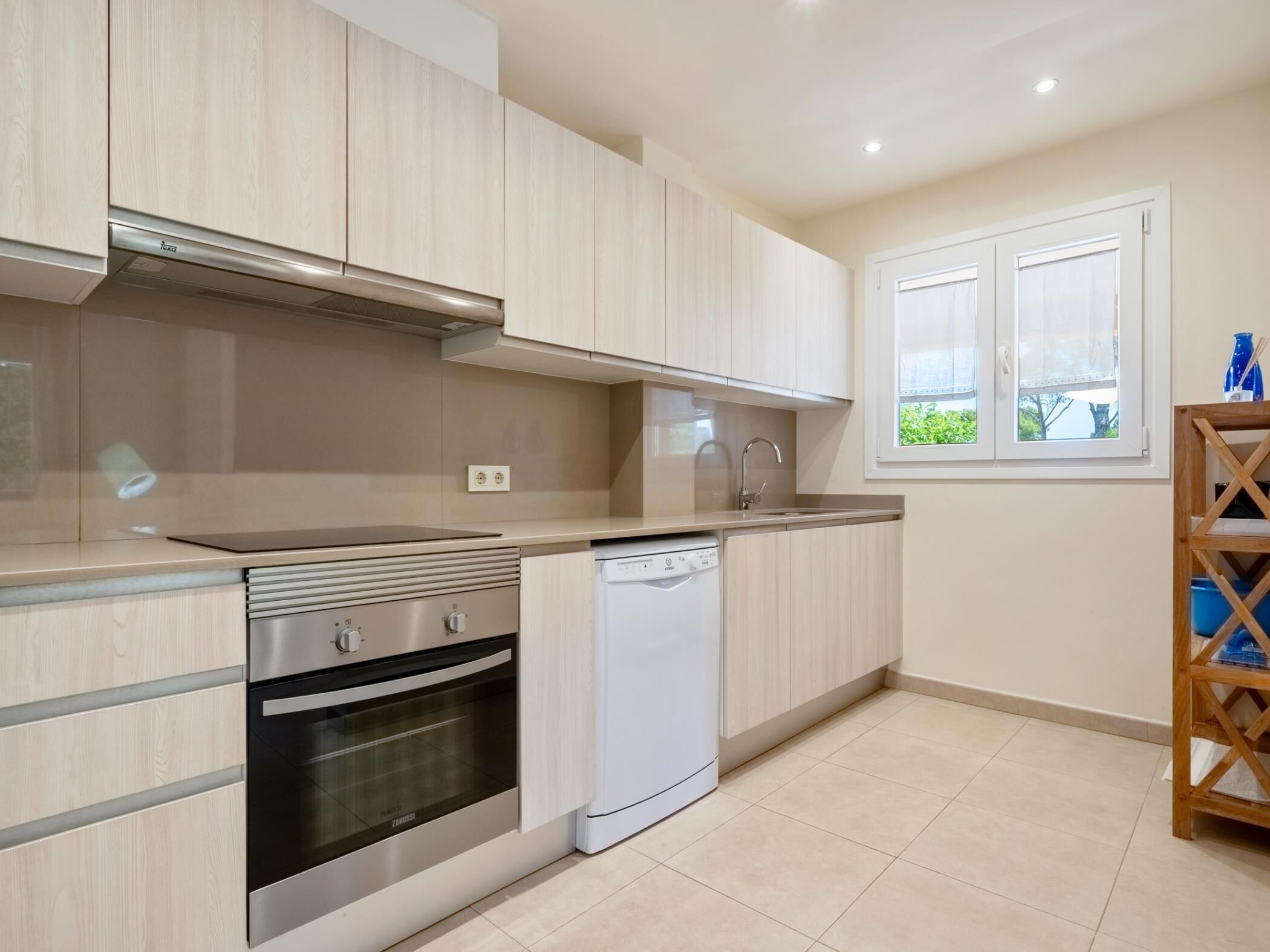Una cocina moderna con armarios de madera clara, electrodomésticos de acero inoxidable y una ventana con vistas a la vegetación.