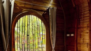 A room with a wooden interior, a round window with vertical bars, a bed with a white mattress, and curtains. - The Backyard Inn (Moalboal)
