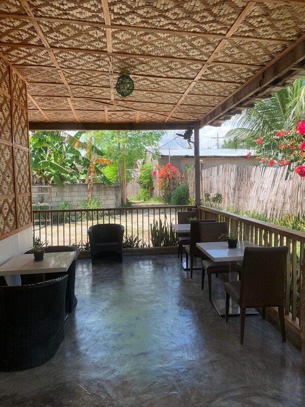 Un patio al aire libre con techo de mimbre, mesas y sillas.