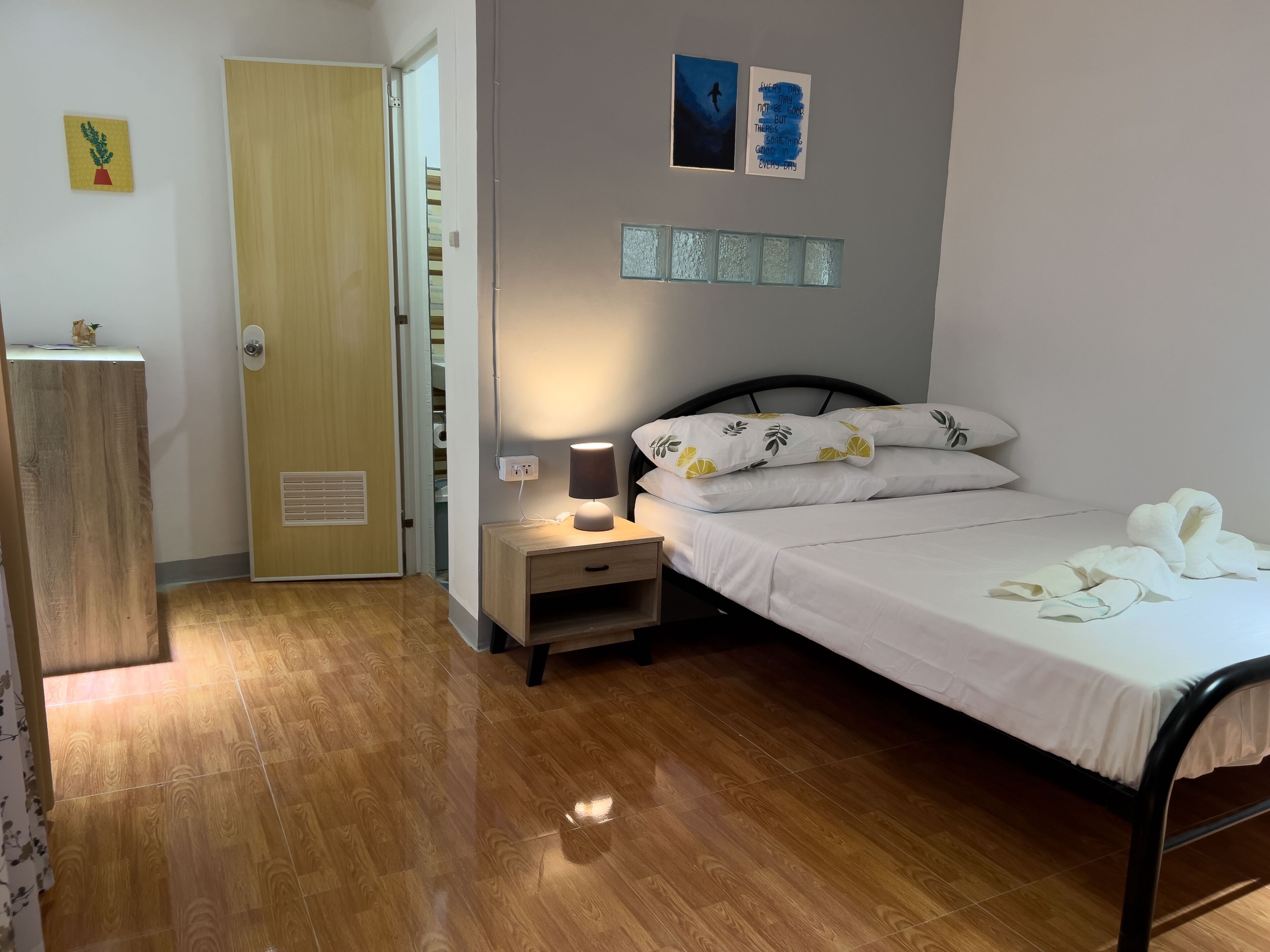 Une chambre avec un plancher en bois, un lit avec une literie blanche, une table de chevet avec une lampe et une porte donnant sur un placard.