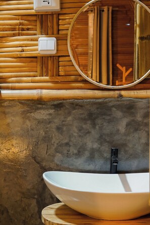 Un baño con pared de madera, un espejo redondo, un lavabo blanco y un perchero para toallas.