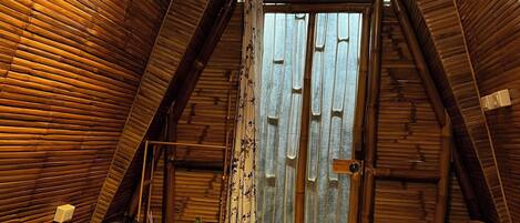 A cozy, wooden-paneled room with a bed, a fan, and a window with curtains.