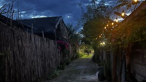 A narrow, unpaved path flanked by wooden fences and vegetation, leading to a building with a sloped roof. - The Backyard Inn (Moalboal)