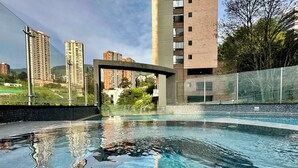 Una piscina con agua cristalina, rodeada de edificios modernos y vistas a un paisaje montañoso.