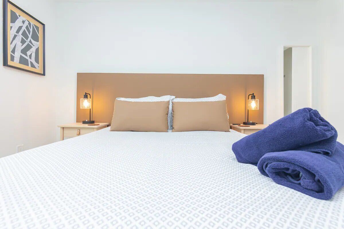 A neatly made bed with a white and beige patterned bedspread, two pillows, and two bedside lamps.