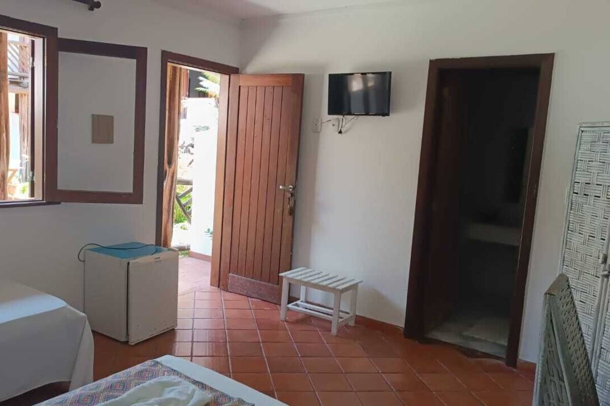 A room with a bed, a small table, a TV mounted on the wall, and a door leading outside.