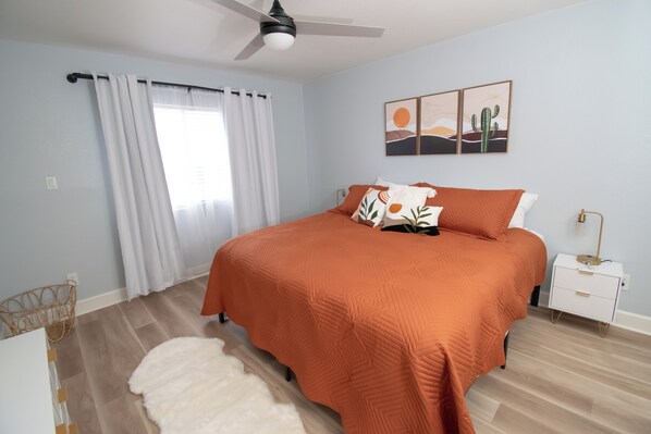 A bedroom with a bed, a nightstand, a ceiling fan, a window with curtains, and a wall art piece. - Endless CASAbilities at this updated, clean Arcadia condo (Phoenix)