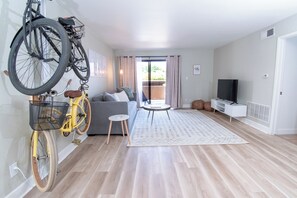 A modern living room with a sofa, a coffee table, a TV, and a bicycle mounted on the wall. - Endless CASAbilities at this updated, clean Arcadia condo (Phoenix)