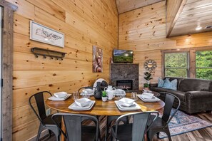 Een houten interieur met een eettafel voor vier personen, een open haard en een bank.