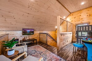 Interior de madeira com televisão, assentos, escada e um espaço de bar.