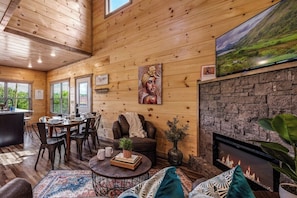 A cozy cabin interior with a dining area, seating, a fireplace, and a television mounted on the wall.
