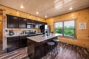 Una cocina moderna con armarios oscuros, encimeras de granito y una isla central con taburetes.