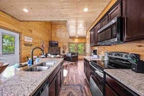 A modern kitchen with granite countertops, stainless steel appliances, and wooden paneling.