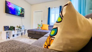 A modern living room with a grey sofa, a flat-screen TV, and a white entertainment unit. -  Ocean-Front Villa~ Beach, Pool, Tennis, 24hr security, Solar, WiFi, playground (Lucea)