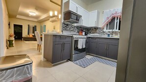 A modern kitchen with grey cabinets, a built-in oven, and a microwave. There is a dining area with a table and chairs visible in the background. -  Ocean-Front Villa~ Beach, Pool, Tennis, 24hr security, Solar, WiFi, playground (Lucea)