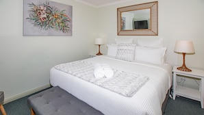 A neatly arranged bedroom with a bed, two bedside tables, a bench, a painting, and a mirror. - Lacy's Place pet Friendly in the Town Center (Mallacoota)