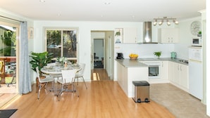 A modern kitchen with white cabinets, a stainless steel range hood, and a dining area with a round table and chairs. - Lacy's Place pet Friendly in the Town Center (Mallacoota)