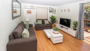 A living room with two sofas, a coffee table, a TV, and decorative plants. - Lacy's Place pet Friendly in the Town Center (Mallacoota)