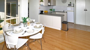 A modern kitchen with white cabinets, a wooden floor, and a dining area with a round table set for four. - Lacy's Place pet Friendly in the Town Center (Mallacoota)