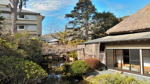 Een traditioneel Japans gebouw met een rieten dak, een vijver met koi karpers en een houten brug.