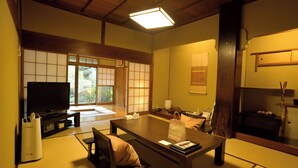 Een traditionele Japanse woonkamer met tatami vloerbedekking, een lage tafel, een bank en een televisie.